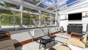 A sunlit room with a large glass window, a black TV on the wall, a wooden bench, and a table with a tray. - Stylish Barn Getaway in Carmarthenshire (Carmarthen)