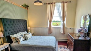 A bedroom with a bed, nightstand, dresser, mirror, window with curtains, and a hanging light fixture.
