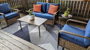 A covered outdoor seating area with wicker furniture, a coffee table, and potted plants.