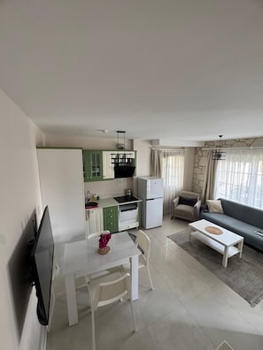 A modern kitchen with green cabinets, a white refrigerator, and a dining area with a white table and chairs. - Olea Alaçatı (Cesme)