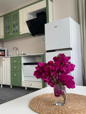 A kitchen with green cabinets, a white refrigerator, and a vase with pink flowers on a table. - Olea Alaçatı (Cesme)