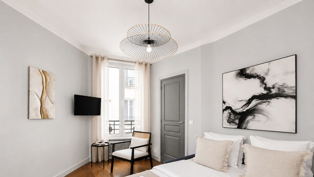 A modern hotel room with a bed, a chair, a small table, a TV, and artwork on the walls. - 1611 Vouillé (Paris)