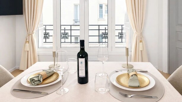 A dining table set for two with a bottle of wine, glasses, and plates. - 1611 Vouillé (Paris)