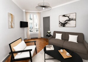 A modern living room with a sofa, a chair, a coffee table, and artwork on the walls. - 1611 Vouillé (Paris)