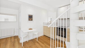 A modern kitchen with white cabinetry, a wooden countertop, and a built-in oven. There is a white stool and a small table with a basket on it. - Host & Stay | The Surf Shack (Saltburn-by-the-Sea)