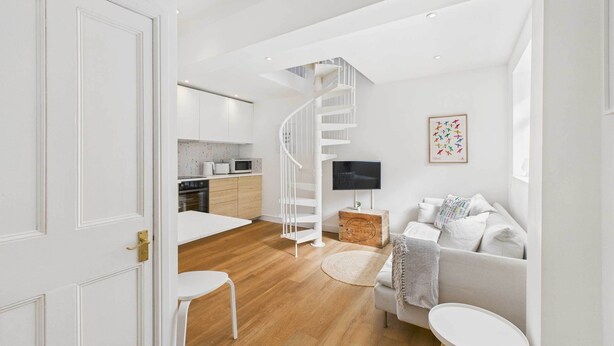A modern living room with a white sofa, a small round table, and a spiral staircase leading to a kitchen. - Host & Stay | The Surf Shack (Saltburn-by-the-Sea)