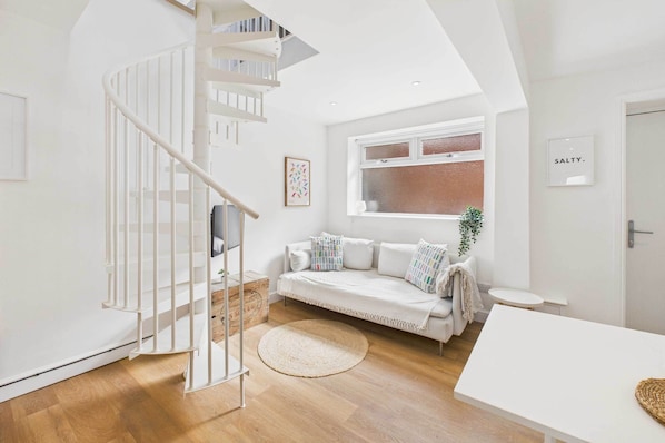 A modern interior with a white staircase, a white sofa set, a round woven rug, and a small round table.