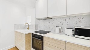 A modern kitchen with white cabinetry, a black oven, a white countertop, a coffee maker, and a microwave. - Host & Stay | The Surf Shack (Saltburn-by-the-Sea)
