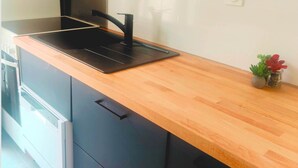 A kitchen with a black countertop, wooden cabinets, and a small plant. - Maison Réthaise 1 city center Garden mix art/flowers (LA FLOTTE)