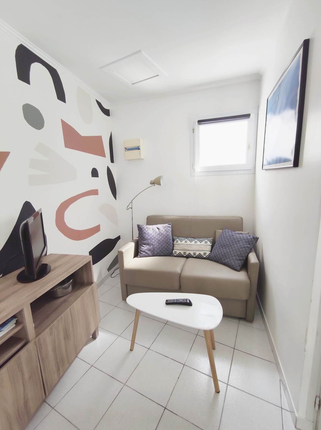 A small, modern living room with a sofa, a coffee table, a TV on a wooden stand, and a wall with abstract art.
