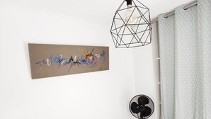 Un dormitorio con cama, lámpara de diseño, ventilador de pared y cortina estampada.