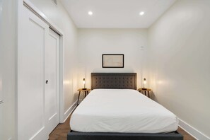 Quarto com uma cama grande, duas mesas de cabeceira com luminárias, um mapa emoldurado na parede e uma porta à esquerda.