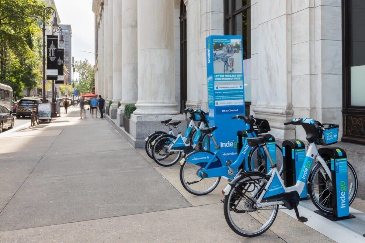 En rad blå och vita elcyklar står uppradade på en trottoar framför en byggnad med klassisk arkitektur.