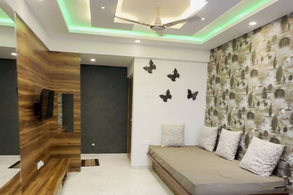 A modern living room with a sofa, a TV mounted on a wooden wall, a ceiling fan, and a decorative wall with butterfly art.