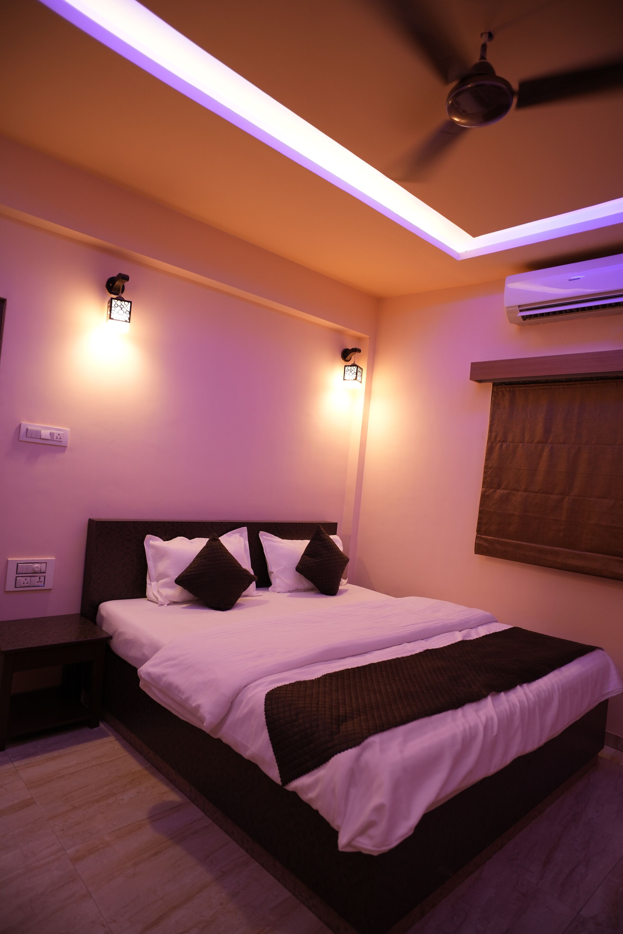 A bedroom with a bed, bedside tables, an air conditioning unit, and a ceiling fan.