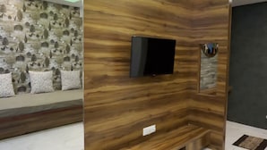 A modern living room with a built-in TV, wooden panel wall, and a stone-patterned wall behind the seating area. - Tara Sitara Luxury Villas (Igatpuri)