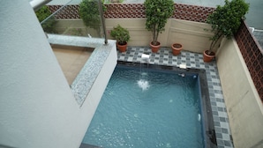 A rooftop swimming pool with a checkered tile border, surrounded by potted plants and a decorative fence. - Tara Sitara Luxury Villas (Igatpuri)