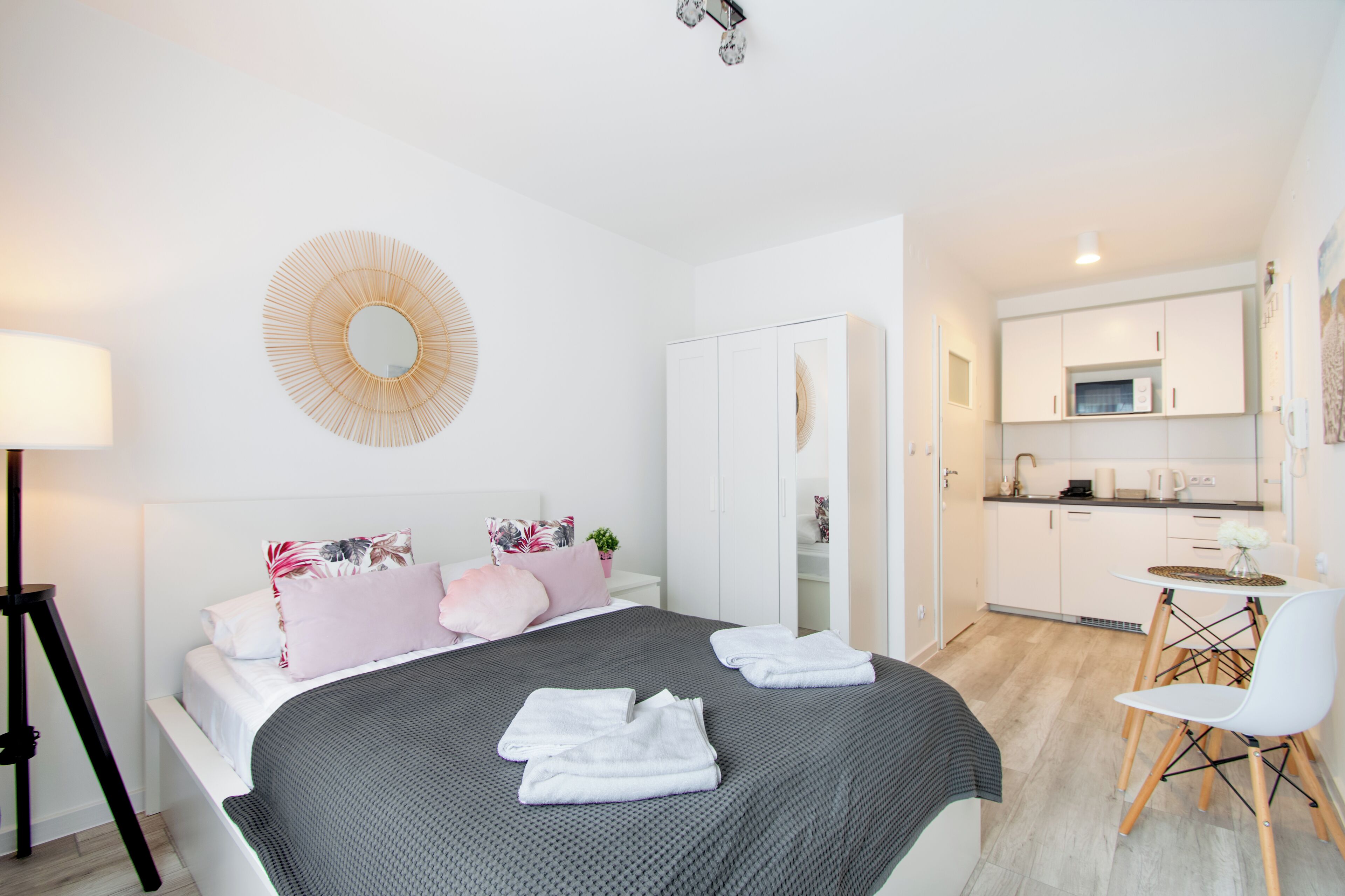 A modern bedroom with a bed, bedside table, and a small kitchenette area.
