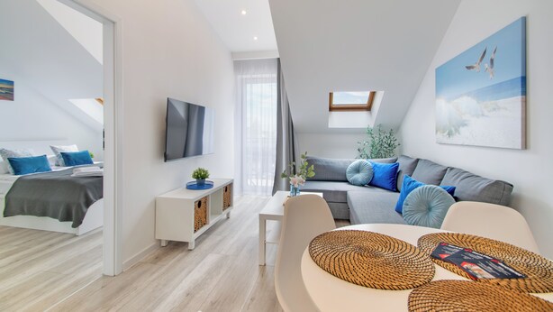 A modern living room with a sofa, a TV, and a dining area. - RentPlanet - Apartament Towarowa (Kolobrzeg)