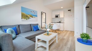 A modern living room with a grey sofa, a white coffee table, and a painting of birds on the wall. - RentPlanet - Apartament Towarowa (Kolobrzeg)