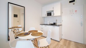 A modern kitchen with white cabinets, a microwave, and a coffee maker. There is a dining table with white chairs and woven placemats. - RentPlanet - Apartament Towarowa (Kolobrzeg)