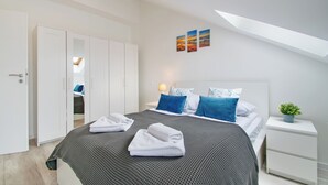 A modern bedroom with a large bed, a wardrobe, a bedside table with a plant, and a skylight. - RentPlanet - Apartament Towarowa (Kolobrzeg)