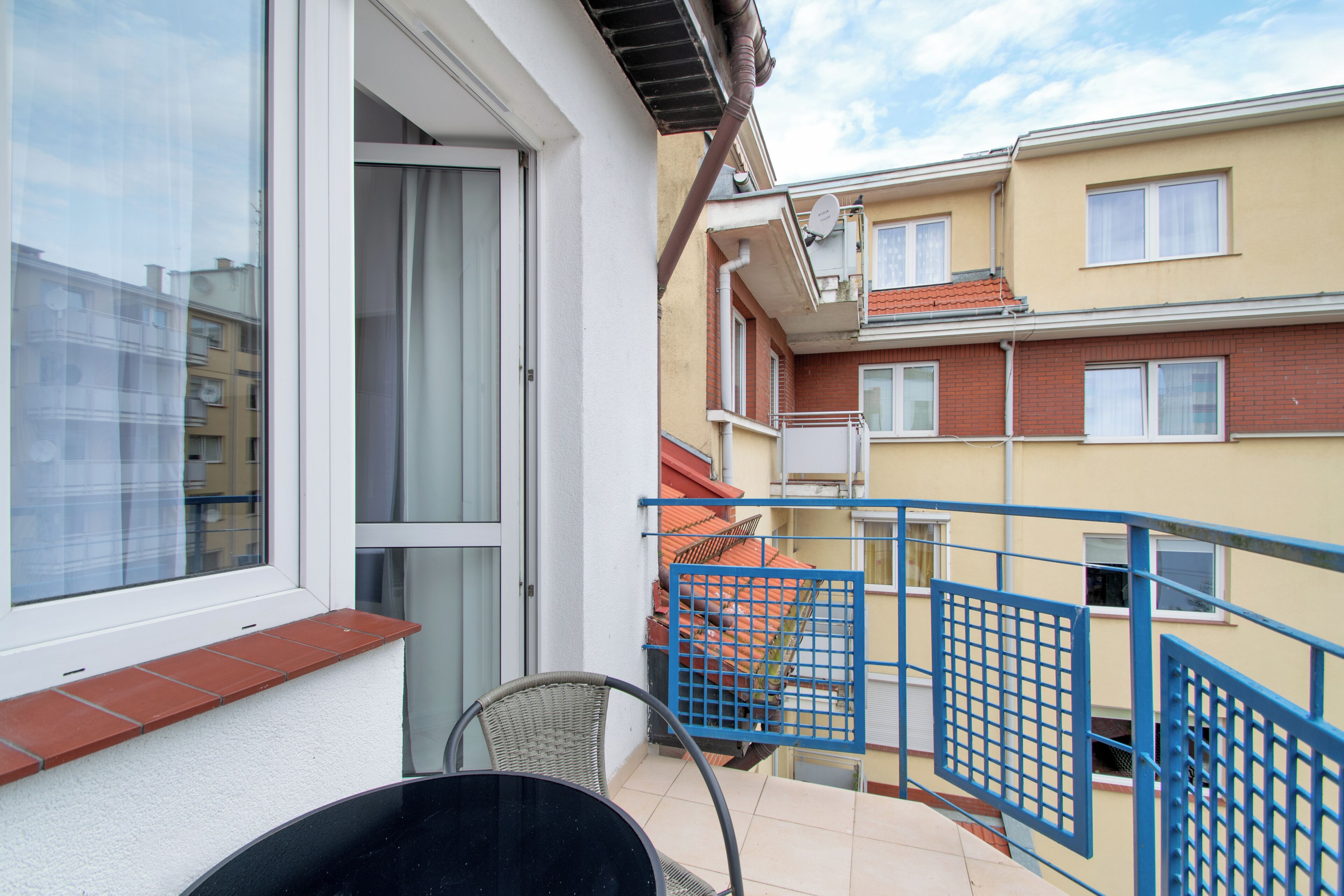 Un balcone con una sedia, un tavolo, ringhiera blu e vista sugli edifici circostanti.