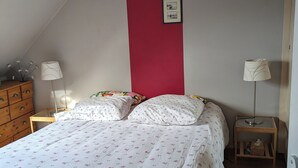 A bedroom with a bed, two nightstands, a dresser, and a red accent wall. - The little sinner's house. (Arromanches-les-Bains)