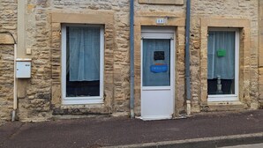 A stone building with a small entrance, a window with a sign, and a satellite dish on the roof. - The little sinner's house. (Arromanches-les-Bains)
