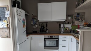 A compact kitchen with white cabinets, a built-in oven, and a refrigerator. - The little sinner's house. (Arromanches-les-Bains)