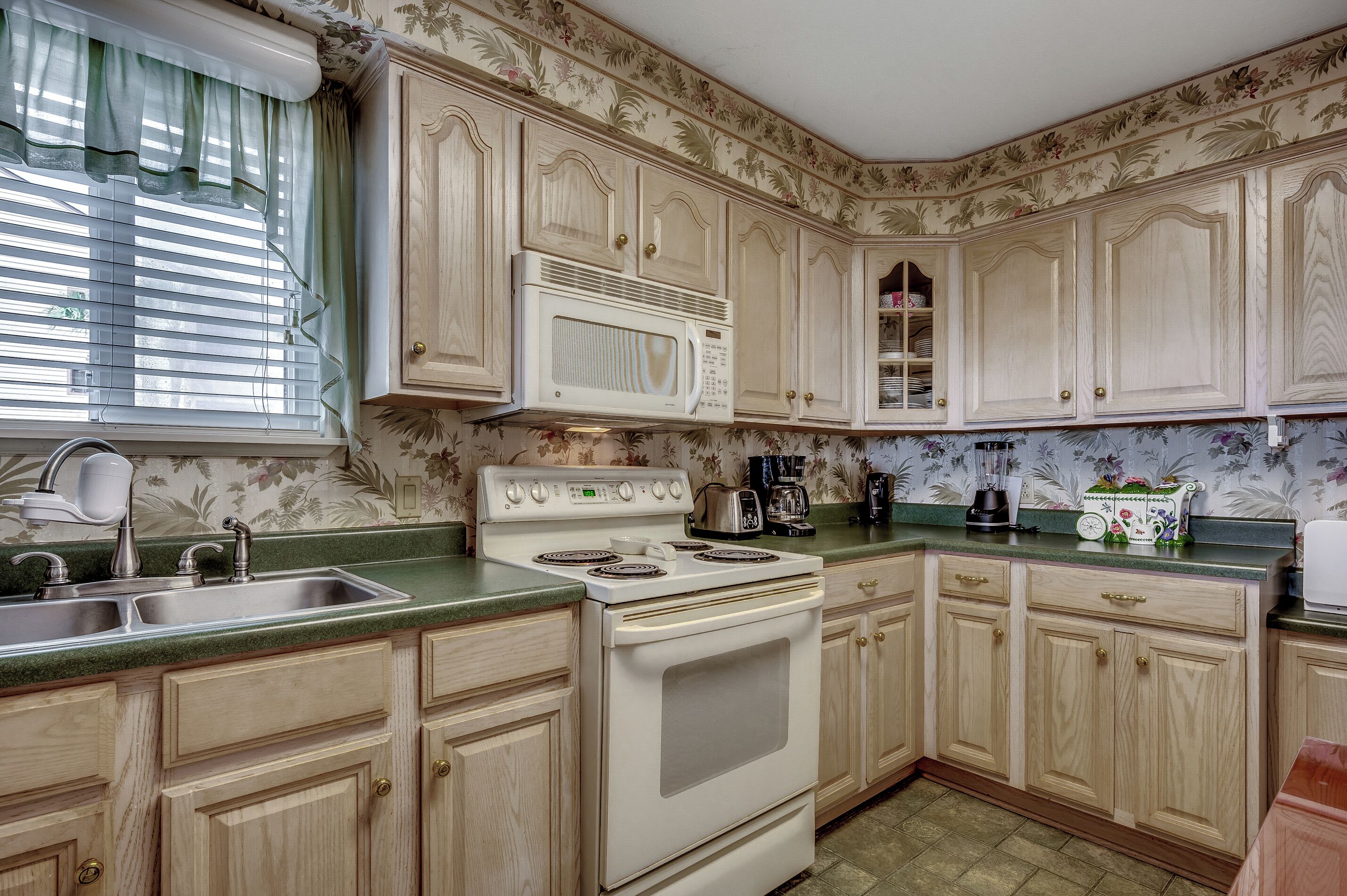 A kitchen with wooden cabinets, a white stove, a microwave, and a sink.