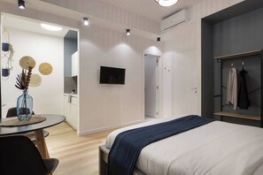 A modern hotel room with a bed, a TV, a wardrobe, and a dining area with a table and chairs. - Trieste Chic Studio: Historic Elegance (Trieste)