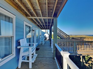Una terrazza in legno riparata con sedie bianche e vista sulla spiaggia.