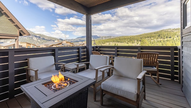 A covered outdoor seating area with a fire pit, chairs, and a view of mountains.