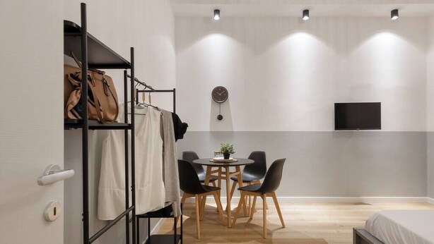 A modern hotel room with a bunk bed, a small dining table with chairs, a flat-screen TV mounted on the wall, and a wooden floor. - Stylish Gem in Historic Trieste for 4 guests (Trieste)