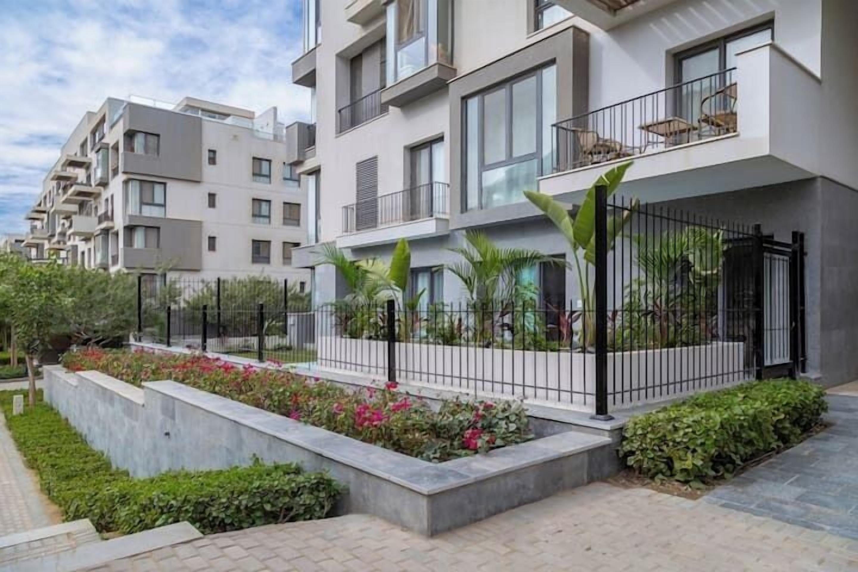Un edificio de apartamentos moderno con balcones, un jardín ajardinado y un camino pavimentado.