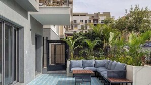 A modern outdoor seating area with a patterned floor, a sofa, and a table. - Kennah Rivera | 2BR Garden Apt, Near EDNC Mall (New Cairo)