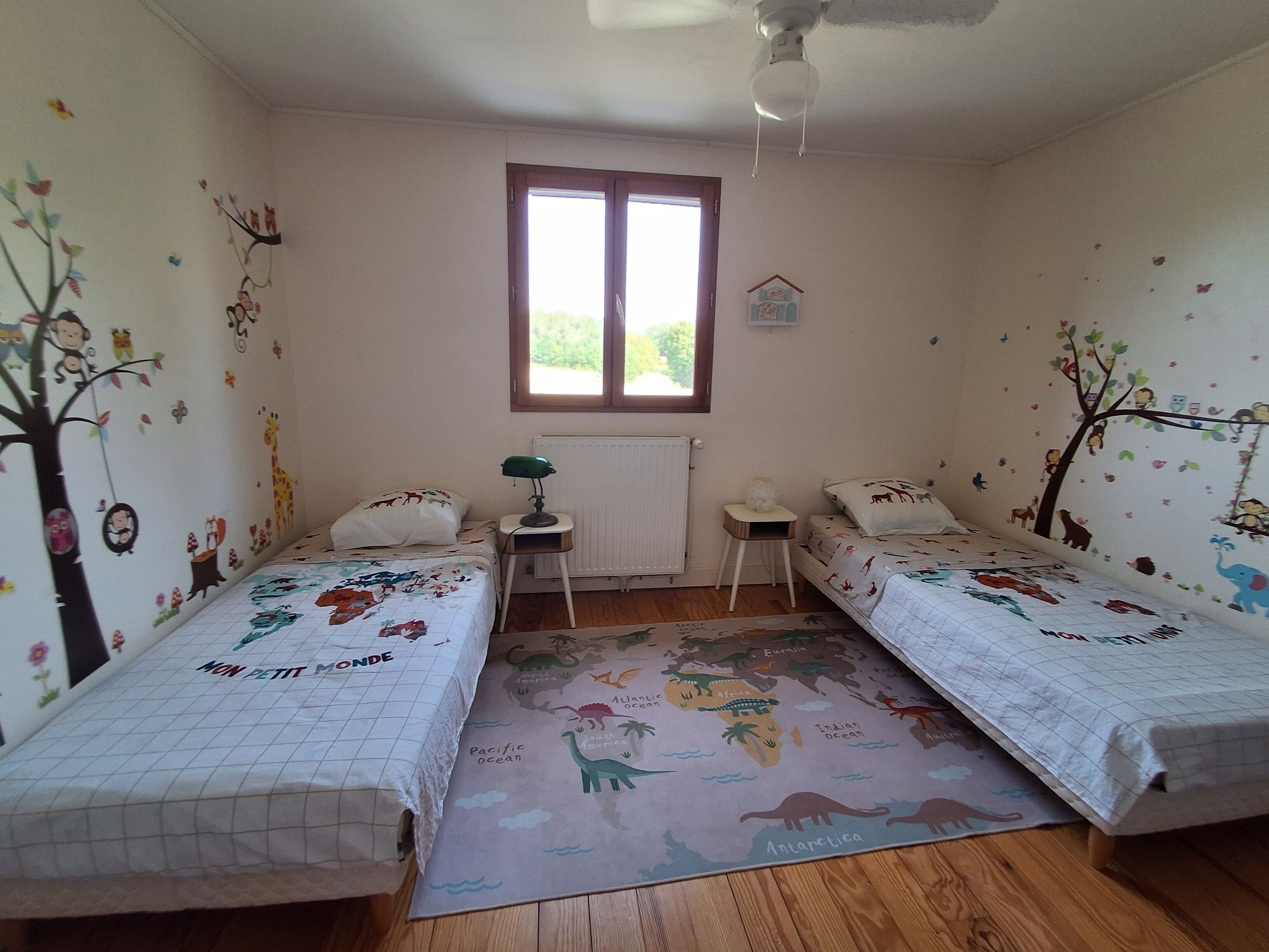 A bedroom with two beds, a window, a radiator, and wall decorations.