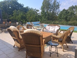An outdoor seating area with wicker furniture and a glass table, overlooking a swimming pool.
