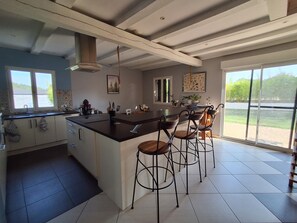 A modern kitchen with a central island, bar stools, and large windows.
