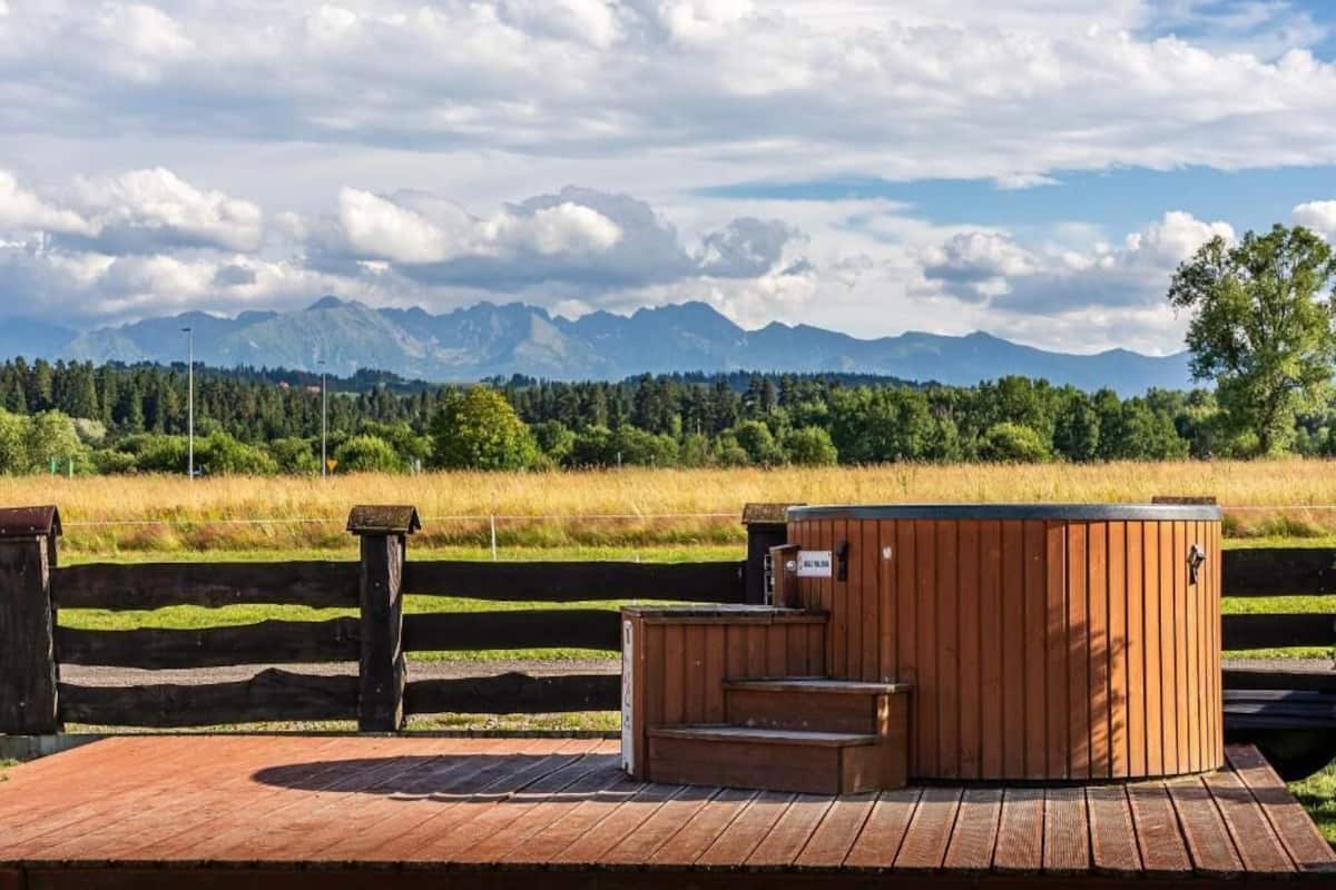 Un jacuzzi de madera en una terraza de madera con vistas a montañas al fondo.