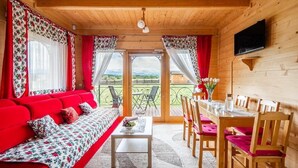 Una habitación acogedora con un sofá rojo, una mesa de comedor con sillas, un televisor en la pared y un balcón con vistas.