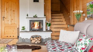 Un interior acogedor de cabaña de madera con chimenea, paredes de madera, un sofá y una escalera.