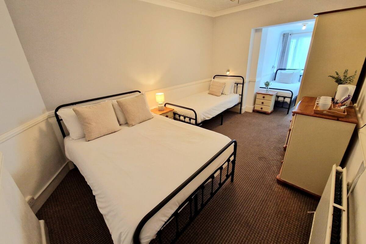 Une chambre avec deux lits simples, une table de chevet avec une lampe, une commode et une fenêtre avec des rideaux.