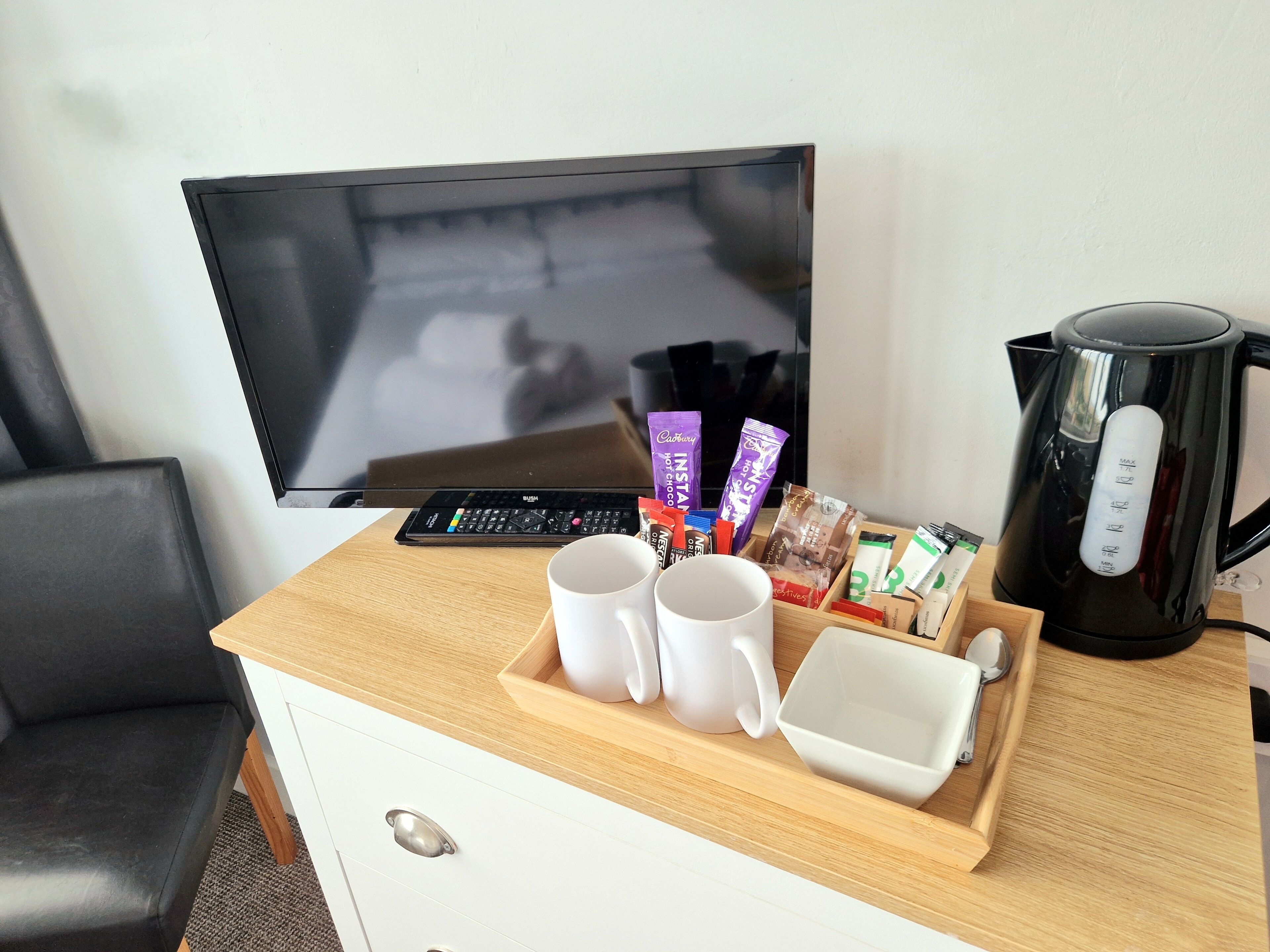 A hotel room with a TV, a coffee maker, a tray with snacks, and a white mug.