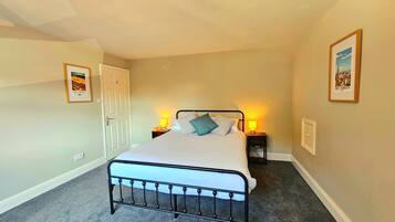 A bedroom with a single bed, two bedside lamps, a door, and two framed pictures on the walls.