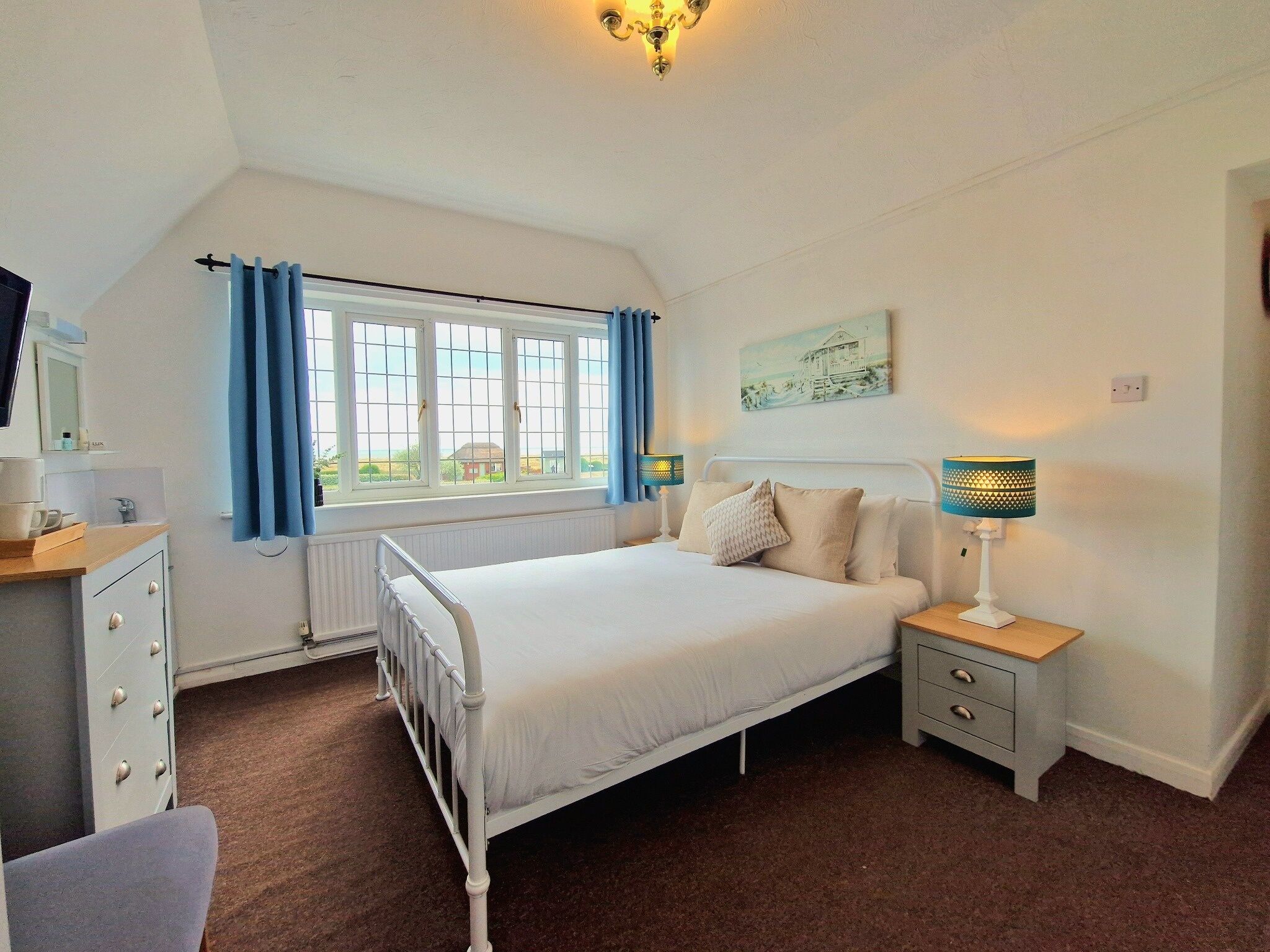 A bedroom with a bed, bedside tables, a window with curtains, a radiator, a wall-mounted lamp, and a painting.