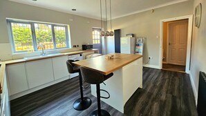 Une cuisine moderne dotée d’un îlot central en bois, de deux tabourets de bar, d’un lave-linge encastré et d’un réfrigérateur.