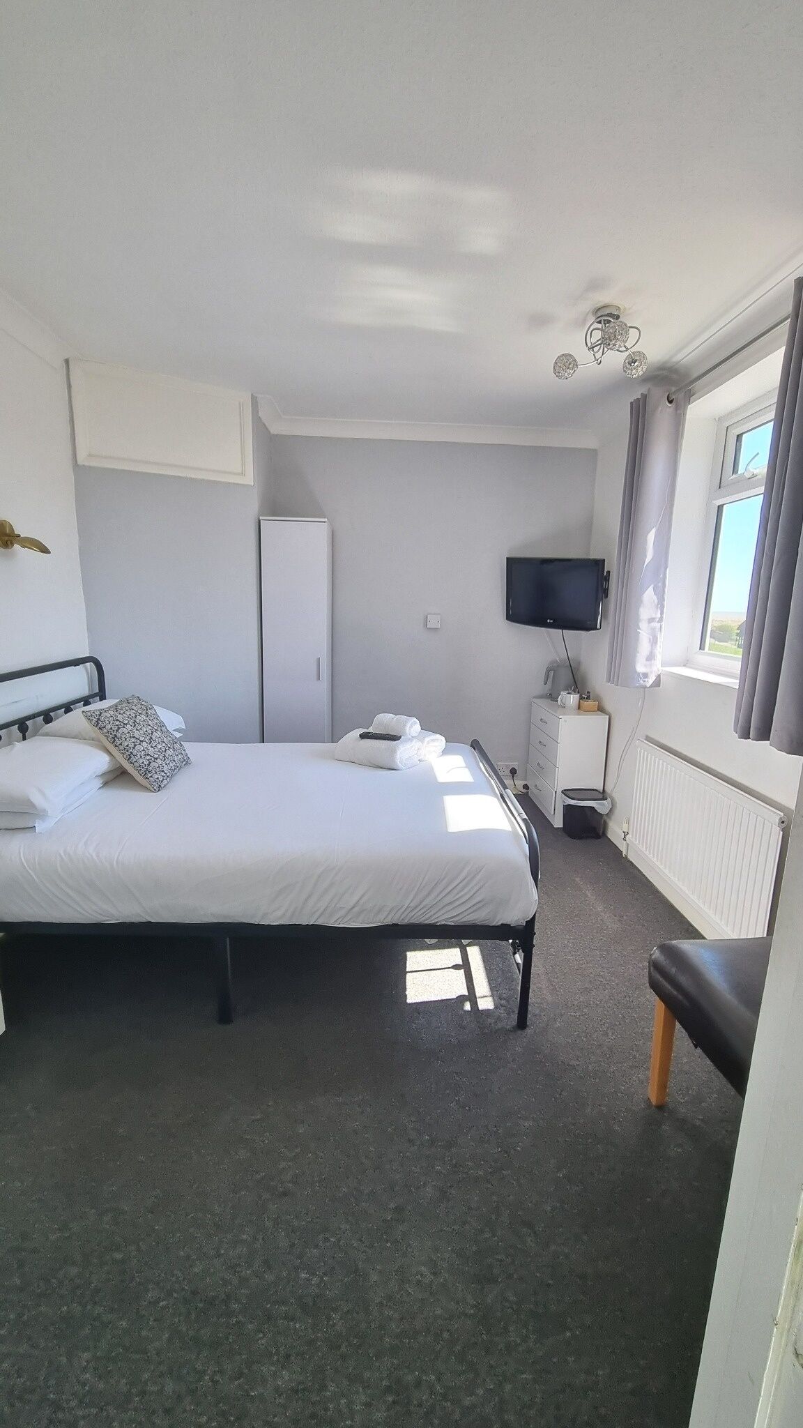 A hotel room with a bed, a television, a dresser, and a window with curtains.