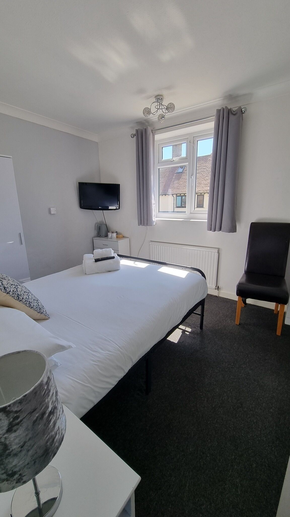 Une chambre d’hôtel avec un lit, une télévision, une chaise, une fenêtre avec des rideaux et un radiateur.